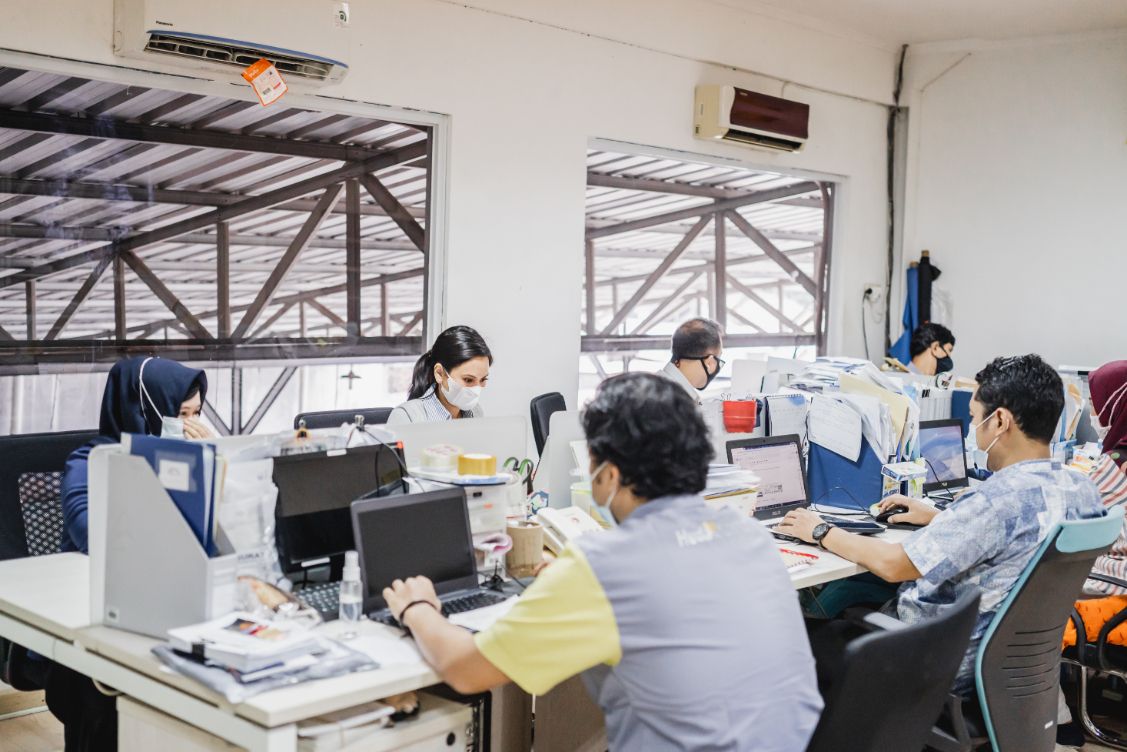 Tim kantor produksi bekerja di meja masing-masing, menjadwalkan dan memantau order berjalan.